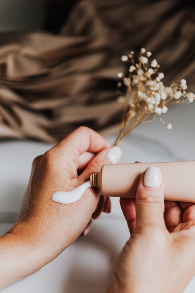 Close-up of a woman applying hand cream from a tube with gentle flowers in the background.